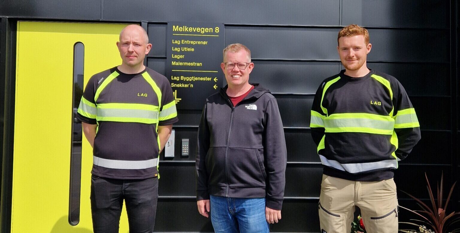 tre menn står under et skilt det står LAG på