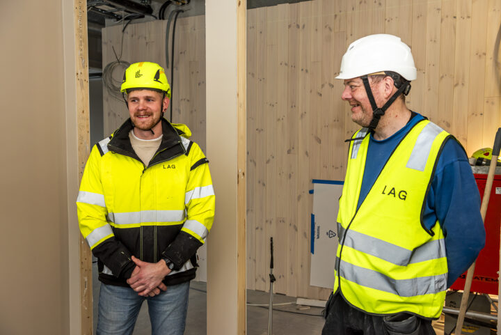 To smilende menn med hjelm og arbeidsklær i samtale