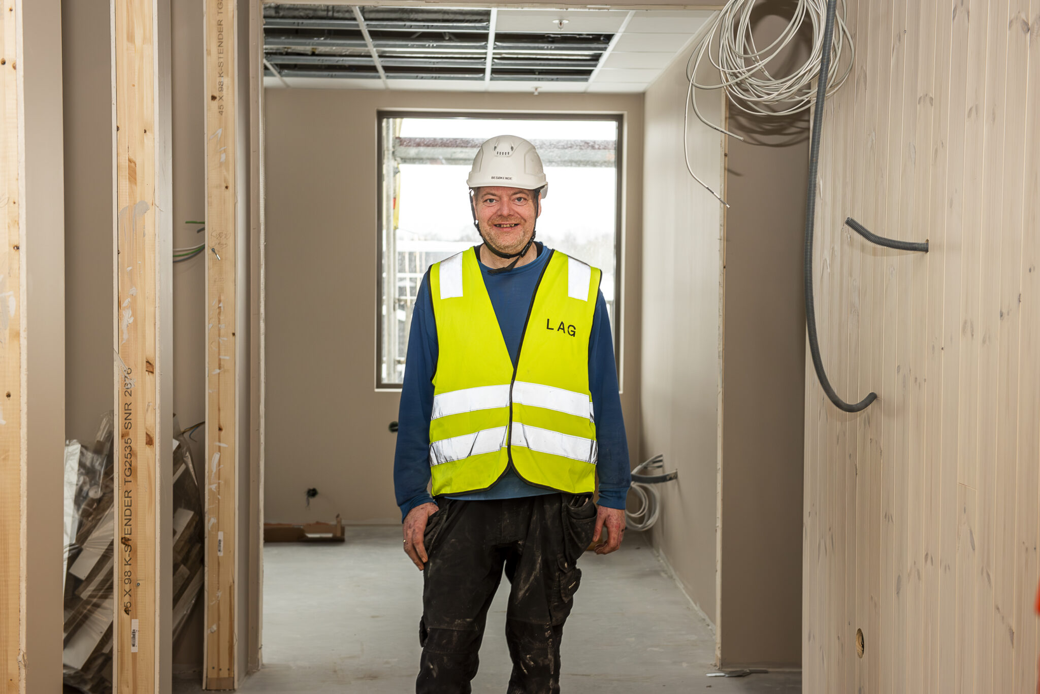 Smilende mann med hjem og vest står på en byggeplass