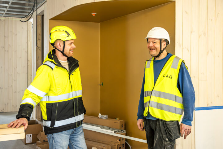 To smilende menn i arbeidsklær står og snakker sammen