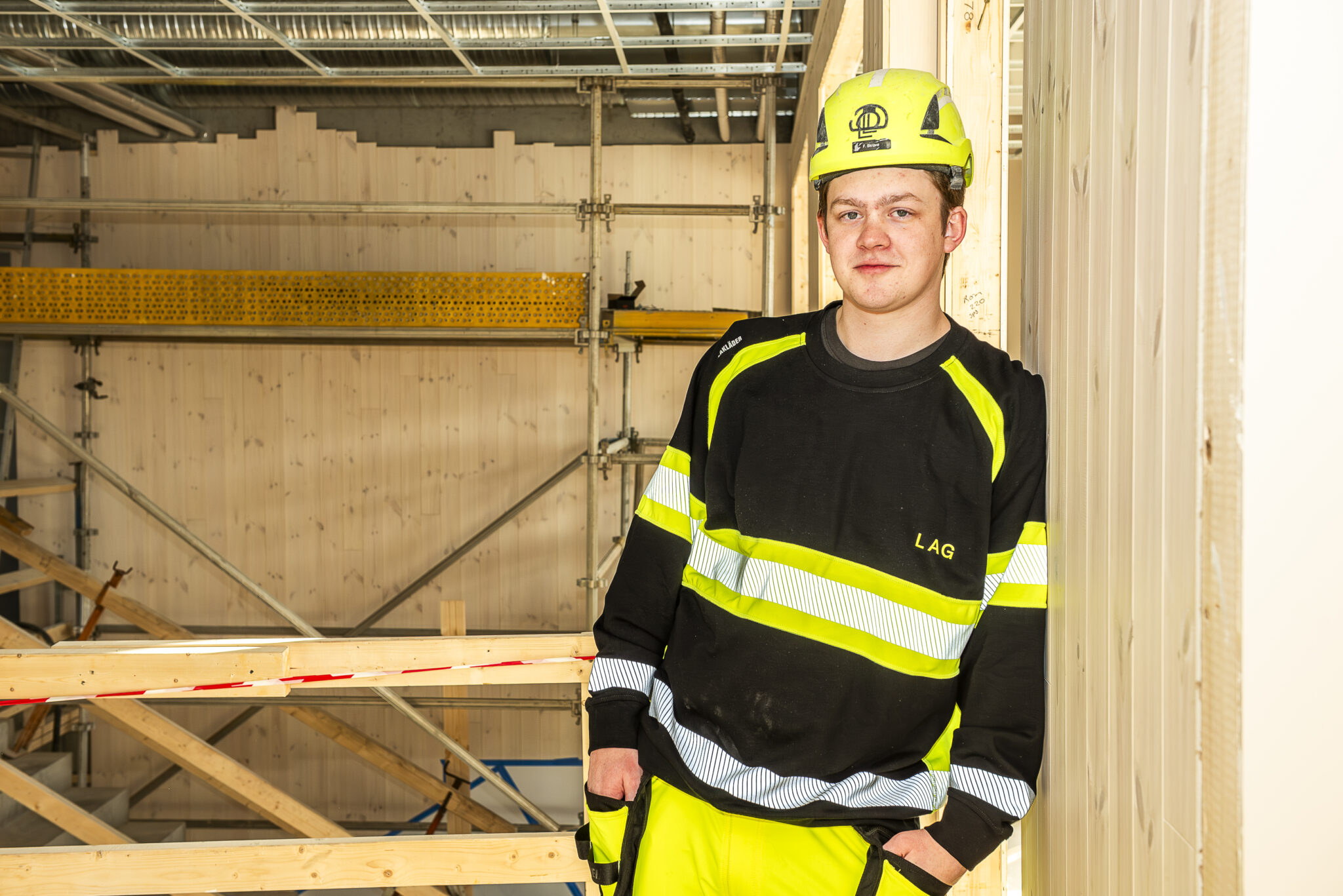Mannlig tømrer i arbeidsklær og med hjelm står inne i et bygg som er under oppføring