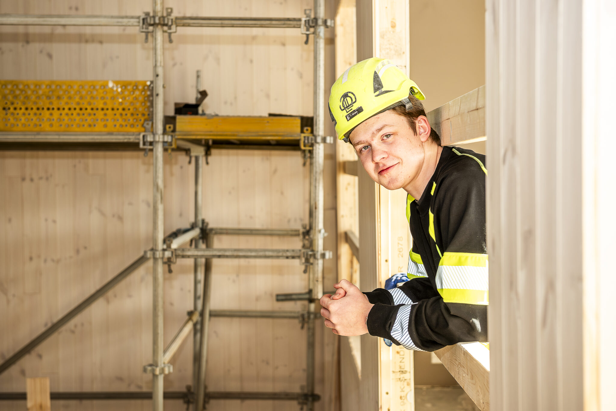 Smilende mann i arbeidsklær og hjelm lener seg frem gjennom et vindu.