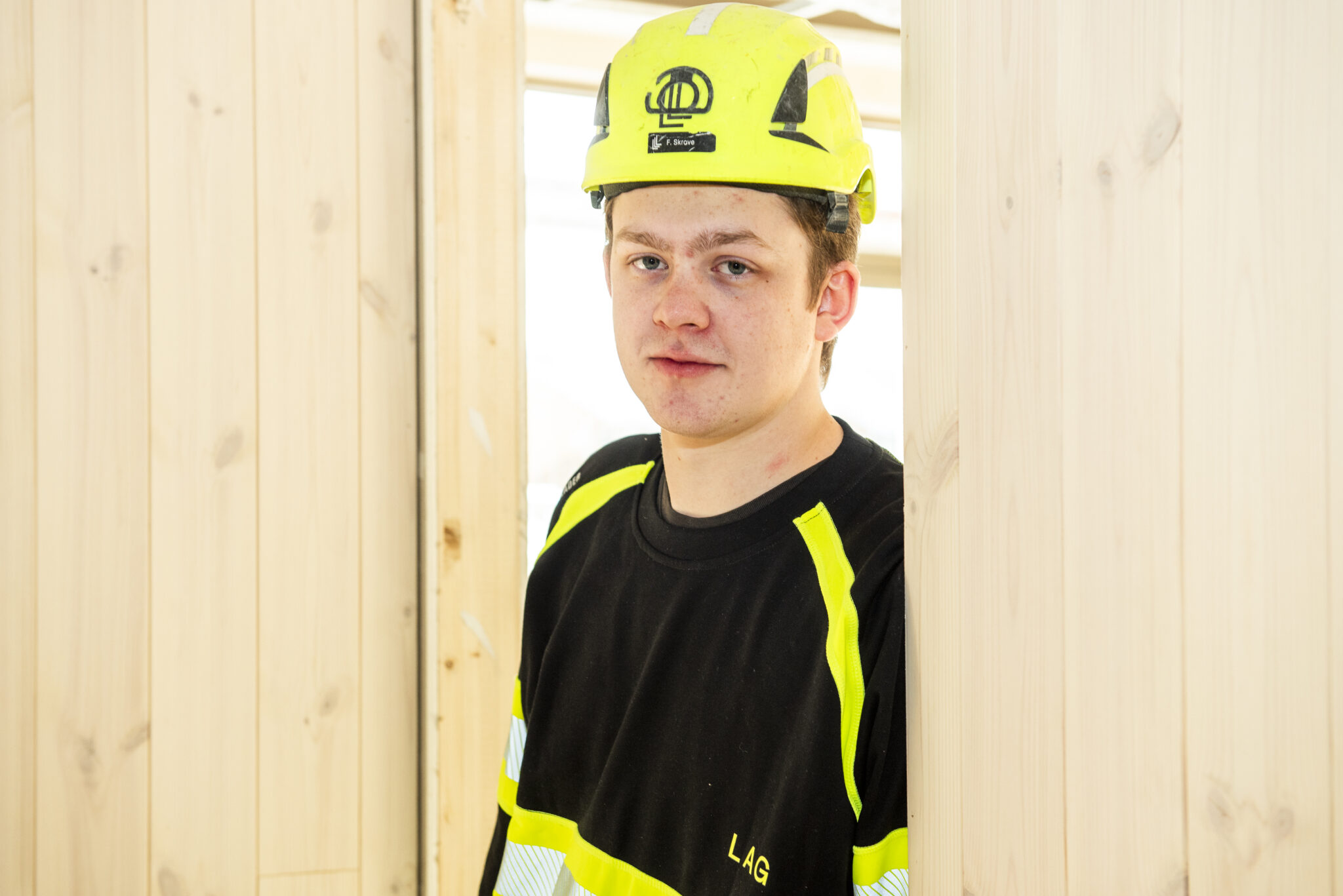 Mannlig tømrer med hjelm lener seg inntil en dørkarm