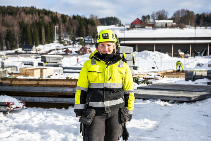 Smilende dame i arbeidsklær og hjelp på en byggeplass