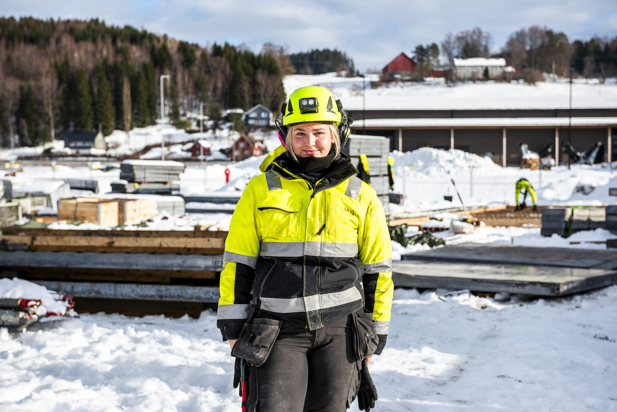 Smilende dame i arbeidsklær og hjelp på en byggeplass