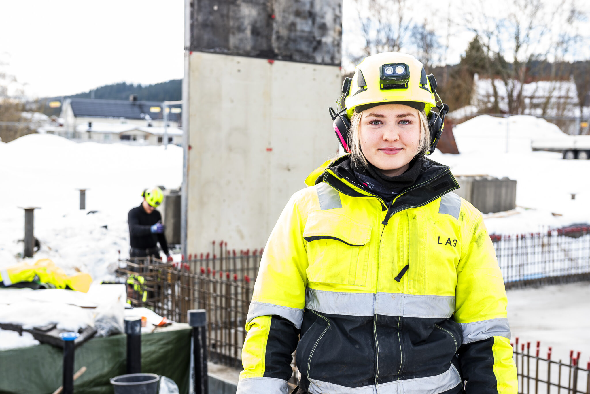 Smilende dame i arbeidsklær og hjelm på en byggeplass