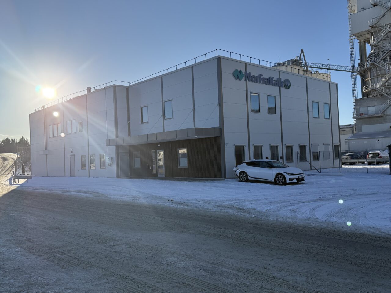 Et hvitt bygg i stål med en bil parkert utenfor. På veggen er logoen til Norfrakalk.