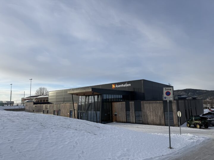 Fasaden på en idrettshall hvit inngangspartiet er i glass og resten er i tre og metall.