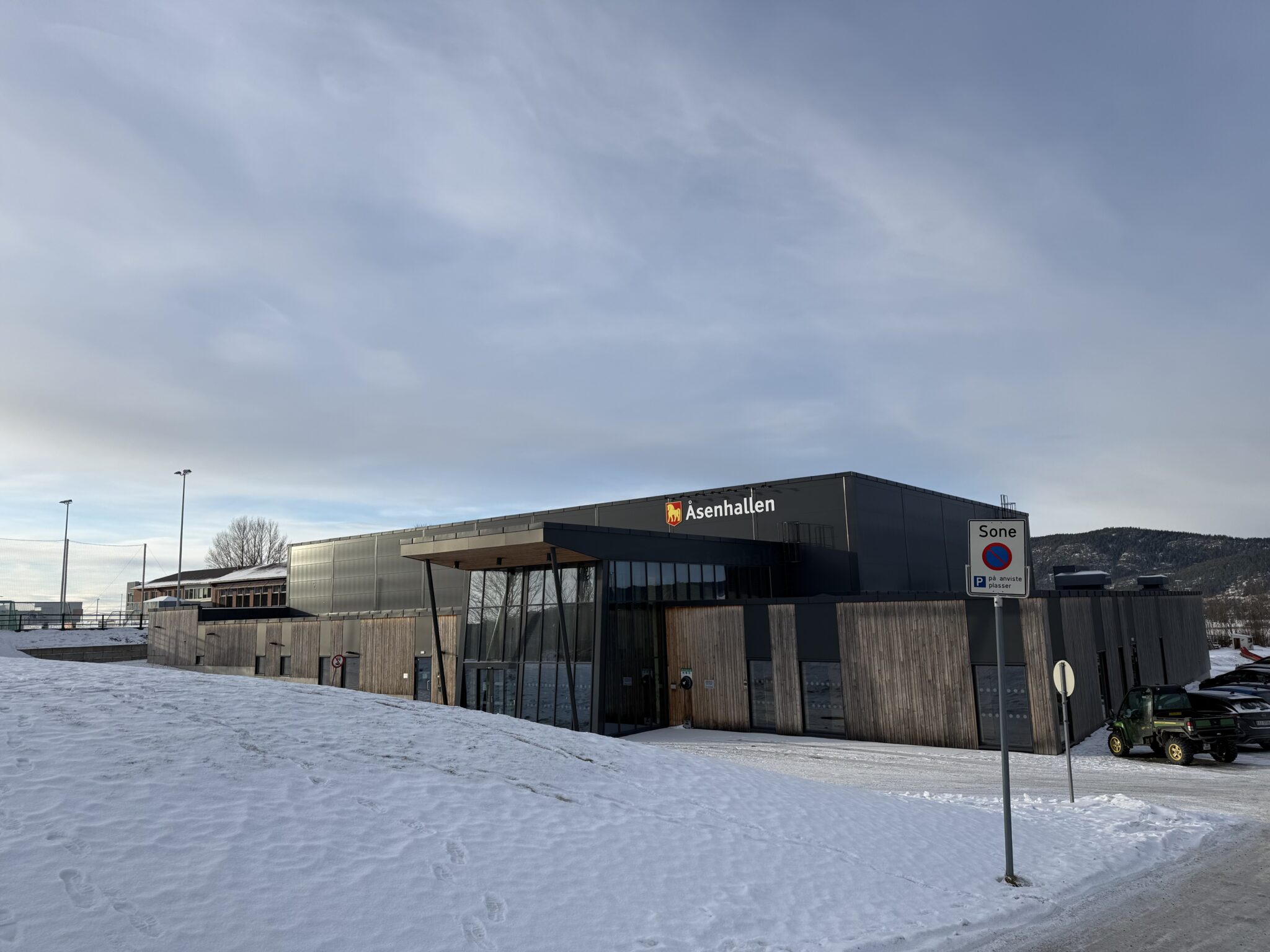 Fasaden på en idrettshall hvit inngangspartiet er i glass og resten er i tre og metall.