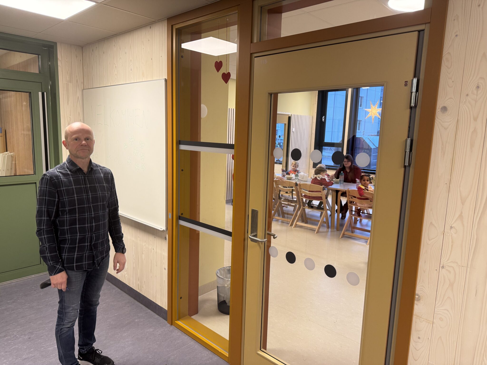 Mann står foran en dør inn til en barnehageavdeling med barn
