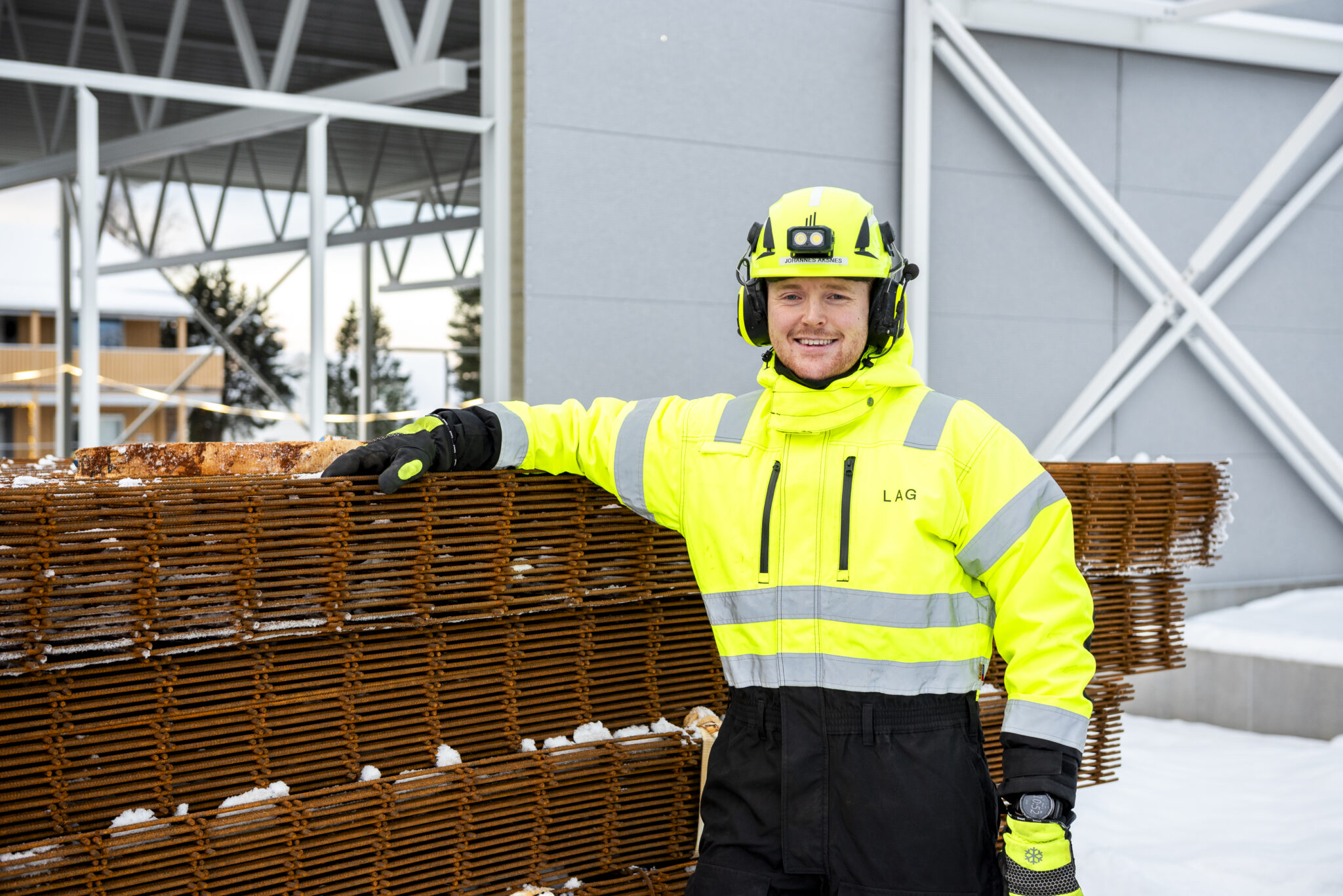 Smilende mann i arbeidsklær stående foran en haug med arbeidsklær