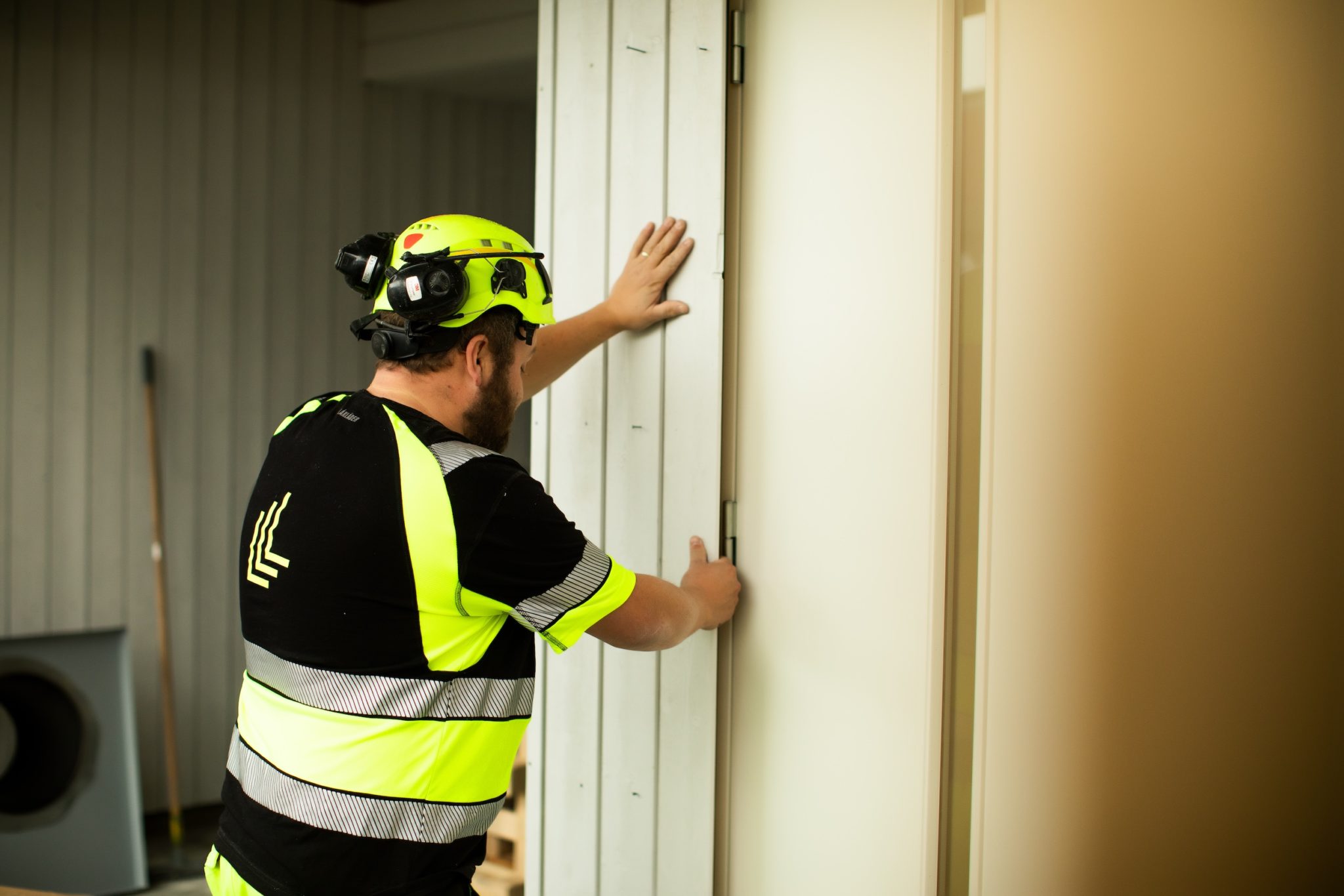 mannlig tømrer som står og legger bordkledning på en vegg