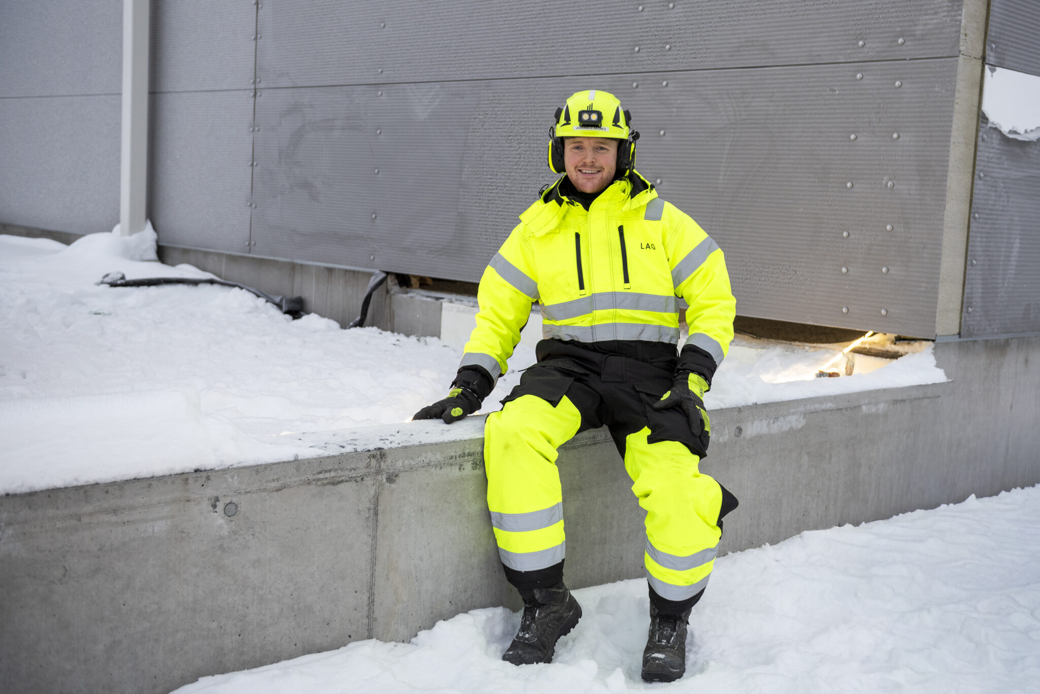 Smilende mann i arbeidsklær sittende på en betongmur