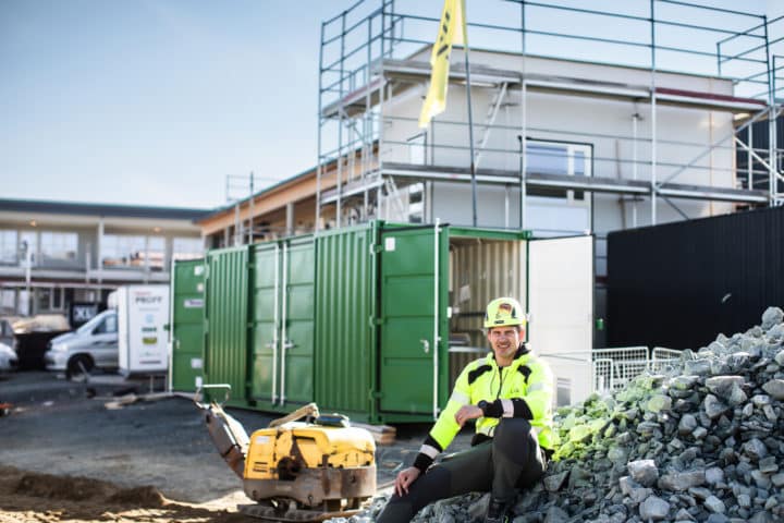 Mann i arbeidsklær sitter på en steinhaug på en byggeplass