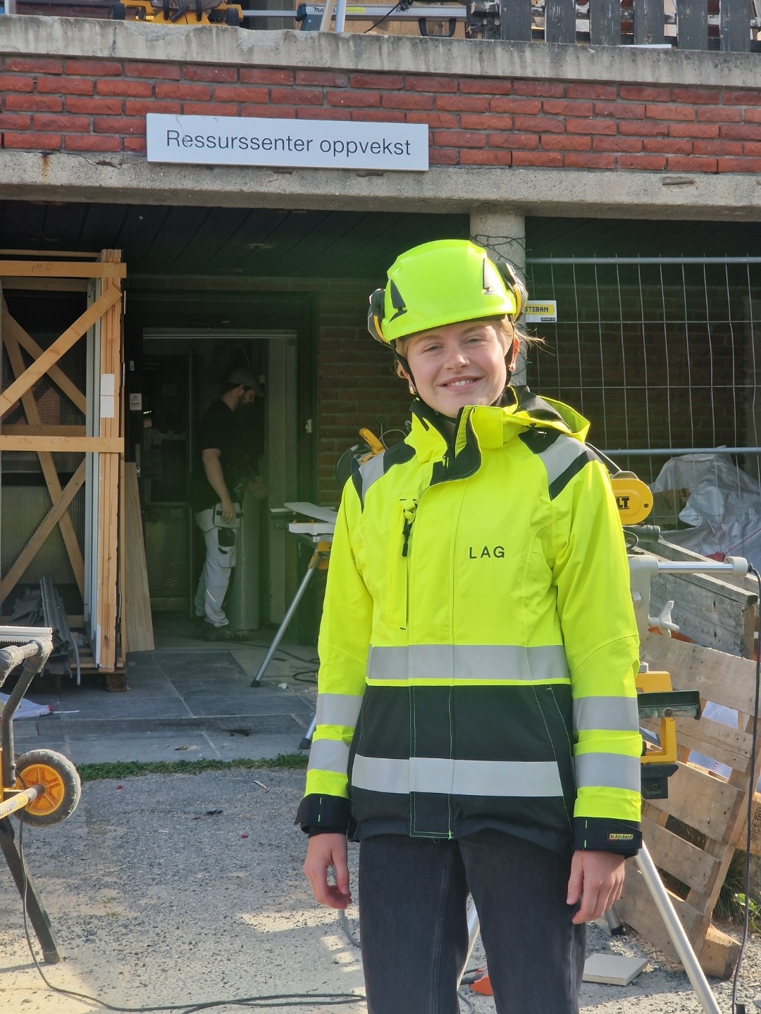 Smilende kvinne i arbeidsklær og hjelm på en byggeplass