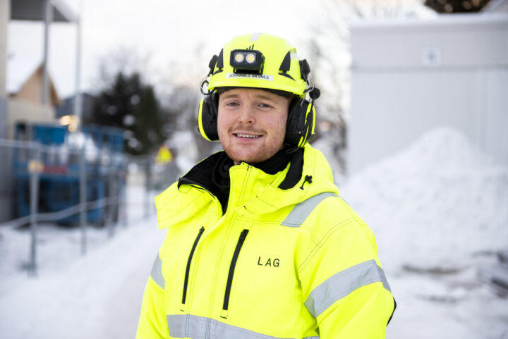 Smilende mann i arbeidsklær står ute i snøen