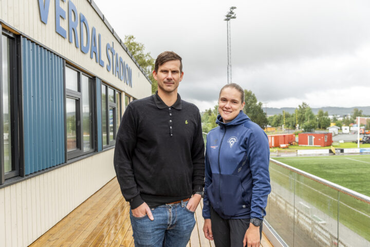 Mann og kvinne står på en verdanda. På veggen bak står det Verdal stadion.
