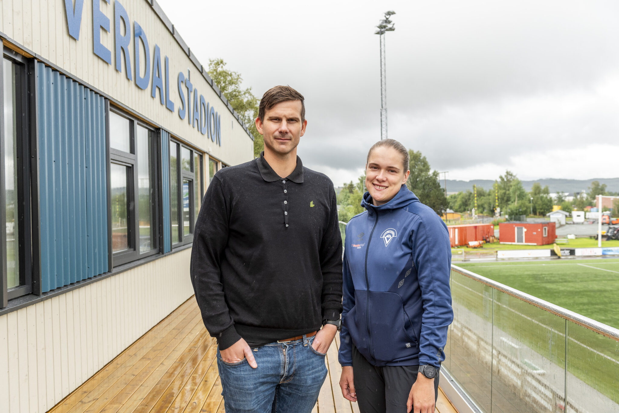 Mann og kvinne står på en verdanda. På veggen bak står det Verdal stadion.