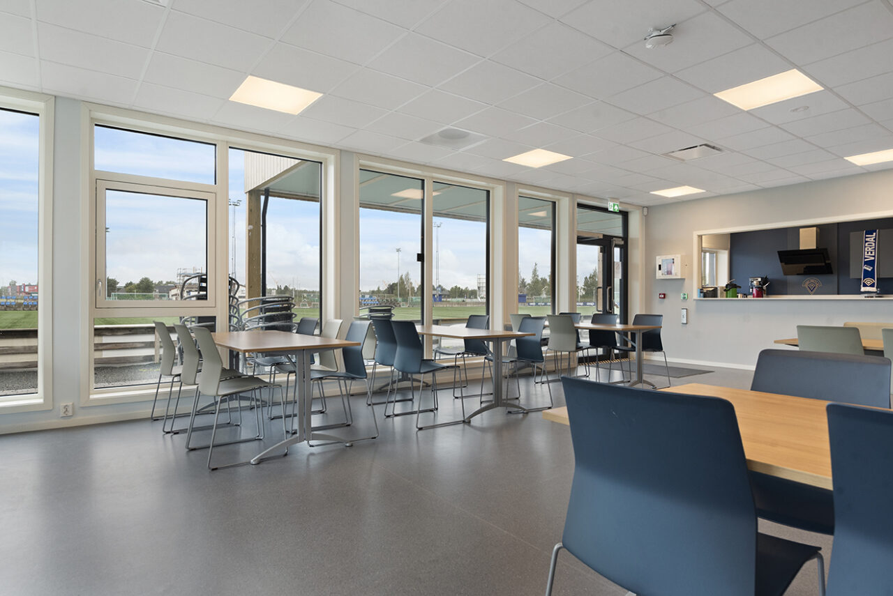 stort åpent rom med store vinduer og bord og stoler